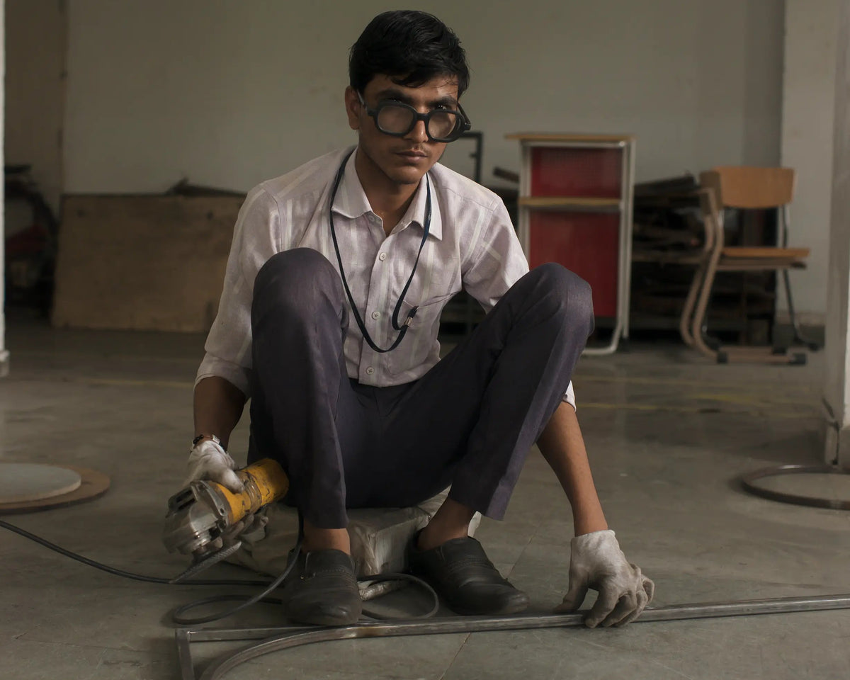 Person wearing goggles and gloves, working with a tool on a metal sheet in an indoor setting.